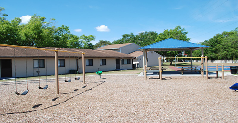 A playground with swings and an awning with picnic tables at Citrus Square Apartments.