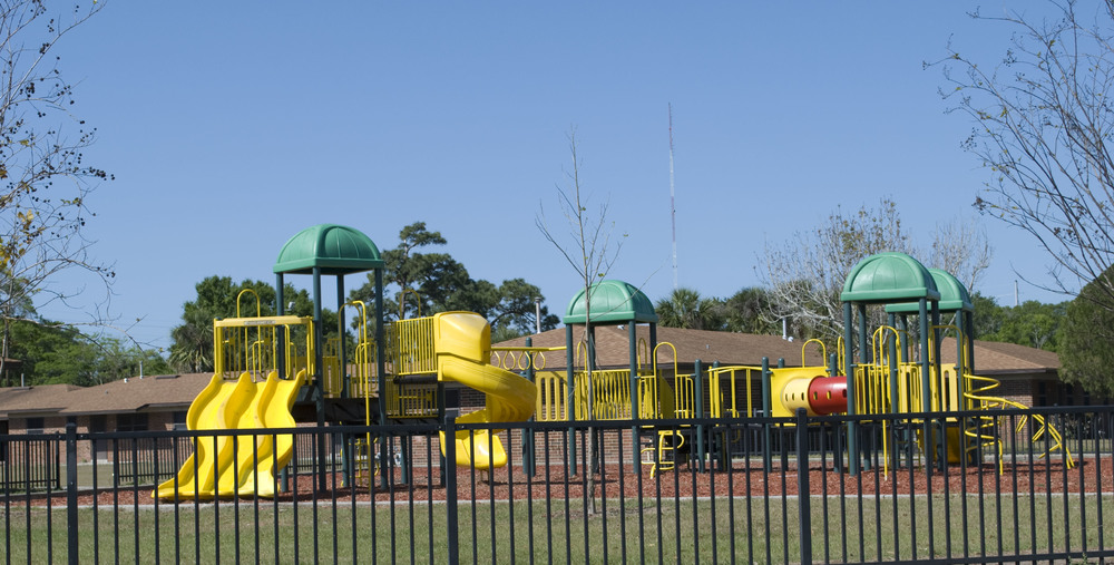 A green and yellow playground behind a fence at Ivey Lane Homes.